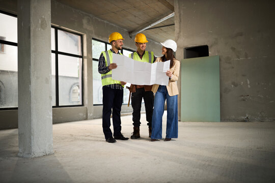 Female interior designer and manual workers cooperating while working on blueprints at construction site