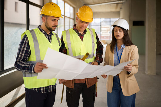 Female project manager and  workers working on plans at construction site.