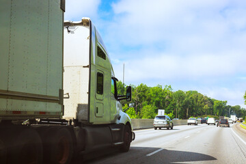 Obraz premium Large truck drives on busy highway with other cars during day trees along roadside.