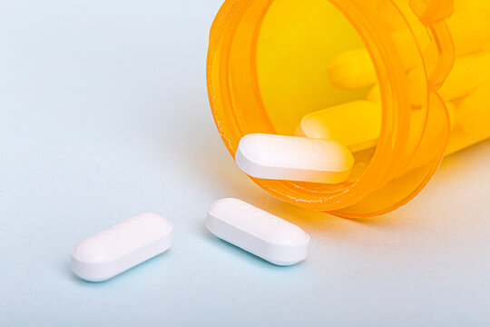 White medicine tablets spilling from an orange prescription bottle on a clean surface. Healthcare, pharmacy, medication, treatment, and medical concept.