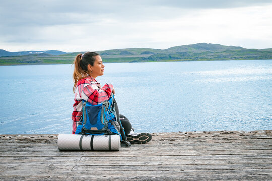 Female backpacker sitting on a wooden pier with heavy rucksack looking at the fjord in Norway