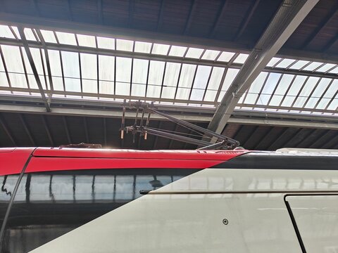 Close-up of a train pantograph on the roof of a modern train under a historic station glass roof