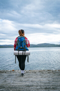 Female backpacker with heavy rucksack walking on a wooden by a fjord in Norway