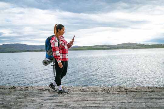 Female backpacker standing on a wooden pier looking at her smartphone screen by a fjord in Norway