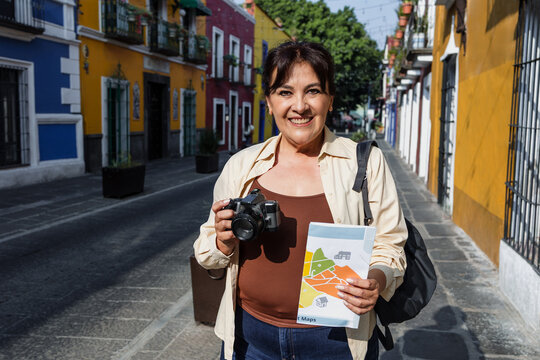 senior latin woman traveling and holding a tourist map in Mexico Latin America, hispanic mature adult or middle age female tourist in colonial city 