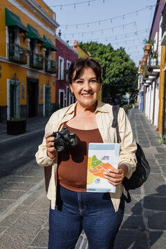 senior latin woman traveling and holding a tourist map in Mexico Latin America, hispanic mature adult or middle age female tourist in colonial city 