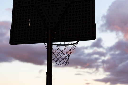 basketball net silhouetted against pastel dusk clouds in sky