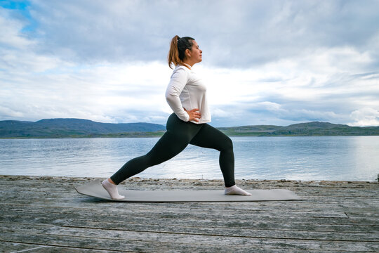 Woman practicing high lunge yoga pose on a mat at a wooden pier by the fjord in Norway