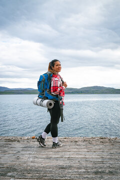 Female backpacker with heavy rucksack walking on a wooden pier looking at camera by a fjord in Norway