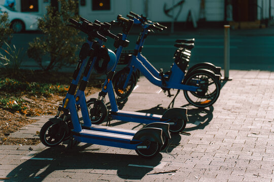 Blue electric scooters and bicycle parked neatly on sunny city sidewalk