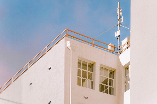White modern building with orange railing and rooftop communication antenna