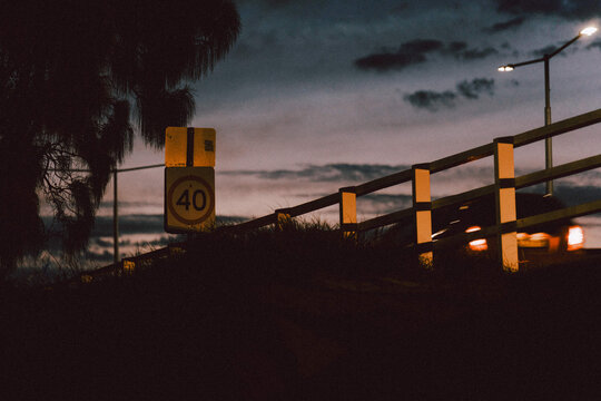 Speed limit sign glowing beside vehicle taillights on darkening evening road