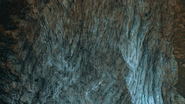 Top down view of textured glacial ice surface with dark soil and intricate frozen cracks motion.