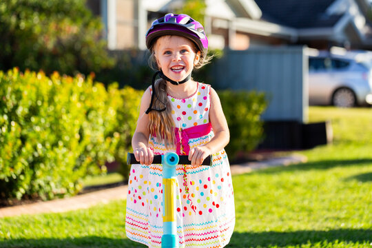 Happy Australian preschooler girl riding scooter in front yard of suburban home