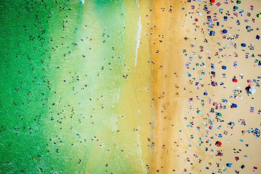 Aerial view of beach with swimmers, umbrellas, and golden sandy shoreline