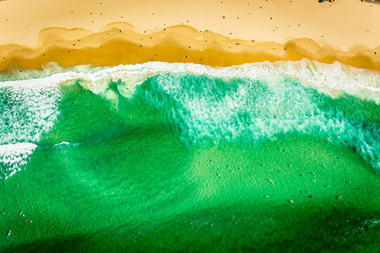 Aerial view of beach with turquoise waves, golden sand, and surfers in Bondi Beach.