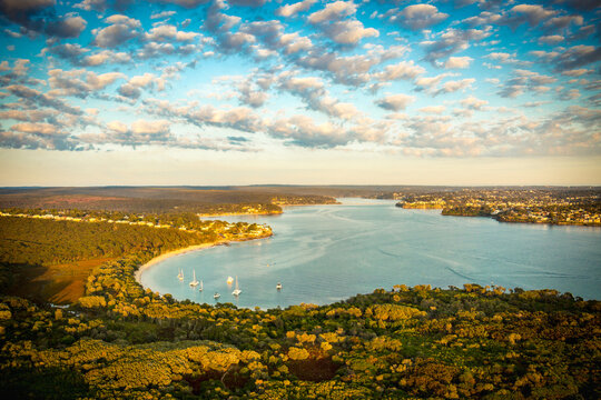 Aerial view of coastal bay with sailboats, houses, and sunset glow over Port Hacking and Bundeena.