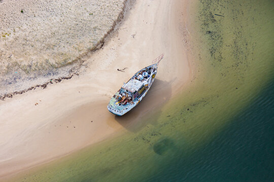 Weathered abandoned boat stranded on sandy shoreline with shallow water
