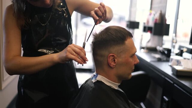 A skilled barber focuses intently as he uses clippers to shape a man's fresh haircut in a lively salon setting filled with the sounds of chatter and buzzing tools in the afternoon light.