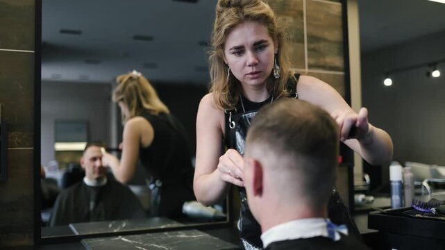 A skilled barber focuses intently as he uses clippers to shape a man's fresh haircut in a lively salon setting filled with the sounds of chatter and buzzing tools in the afternoon light.