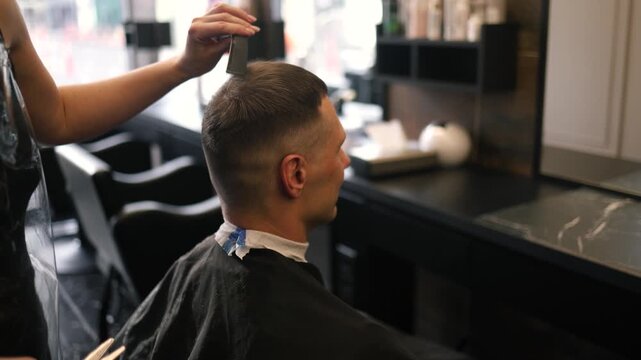 A skilled barber focuses intently as he uses clippers to shape a man's fresh haircut in a lively salon setting filled with the sounds of chatter and buzzing tools in the afternoon light.