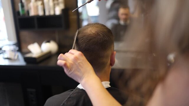 A skilled barber focuses intently as he uses clippers to shape a man's fresh haircut in a lively salon setting filled with the sounds of chatter and buzzing tools in the afternoon light.