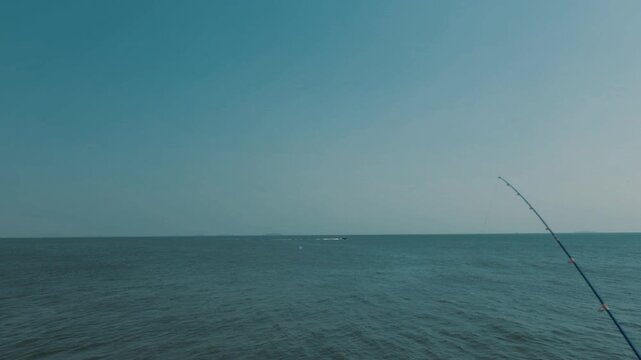 Calm ocean scene with an extended fishing rod tip against a blue sky background, perfect for outdoor, fishing, travel content.