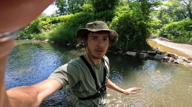 Male outdoor vlogger speaking to camera while standing in a forest stream, fishing lifestyle and influencer concept vlog.