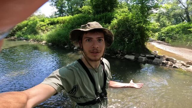 Male outdoor vlogger speaking to camera while standing in a forest stream, fishing lifestyle and influencer concept vlog.