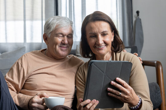 Senior couple tablet home sofa smile tea elderly technology sharing relaxed digital moment together in cozy living room