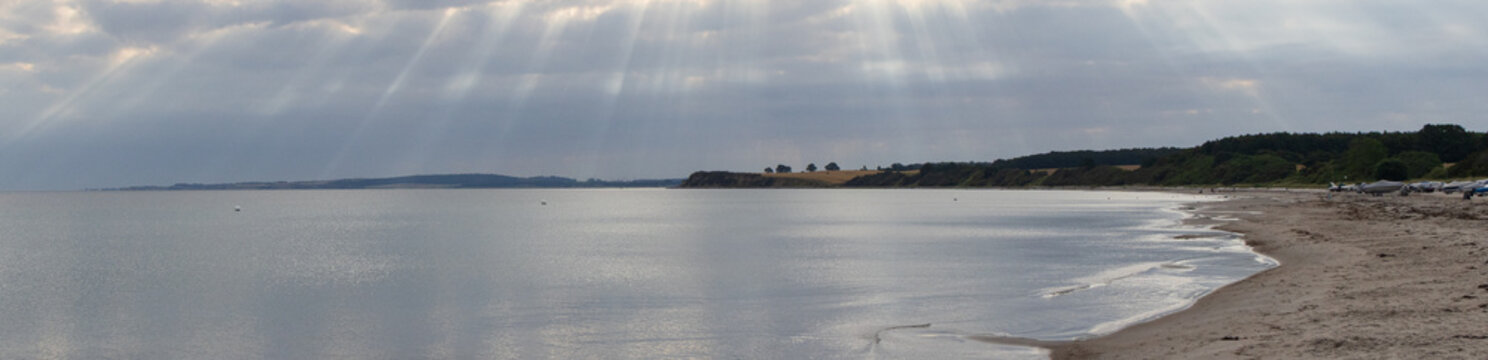 Panoramic view of Sehlendorf beach on the Baltic Sea with sunbeams piercing through the clouds