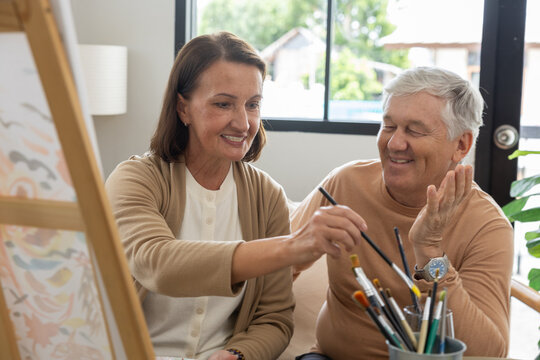 Senior couple art painting brush canvas home creativity smiling hobby retirement joyfully making artwork together in bright cozy studio