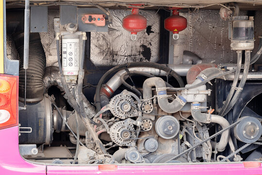 Open rear engine bay of a commercial passenger bus showing dual alternators, drive belts, fuel filter, and cooling system components.