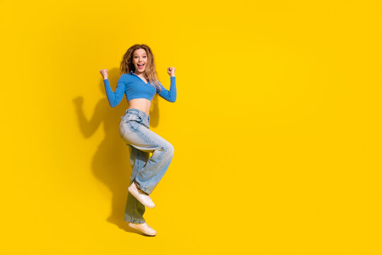 Joyful young woman jumping with enthusiasm against a vibrant yellow background, expressing excitement and energy in trendy casual attire.