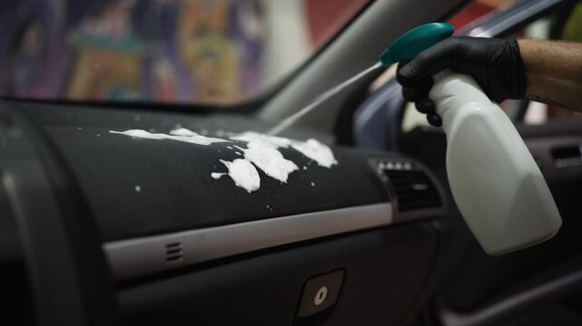 Auto detailer wear protective gloves spray cleaning foam onto car dashboard for deep cleaning and interior restoration. Automotive detailing, vehicle maintenance and professional car care concept