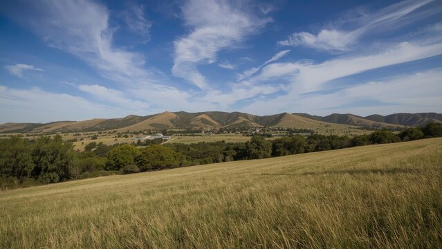 Expansive landscape with grassy fields, rolling hills, and a bright blue sky with clouds.