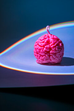 Creative pink brain-shaped candle illuminated by colorful rainbow light on a dark background. Surreal Halloween decoration, spooky home decor, neuroscience concept, creativity, imagination and modern 