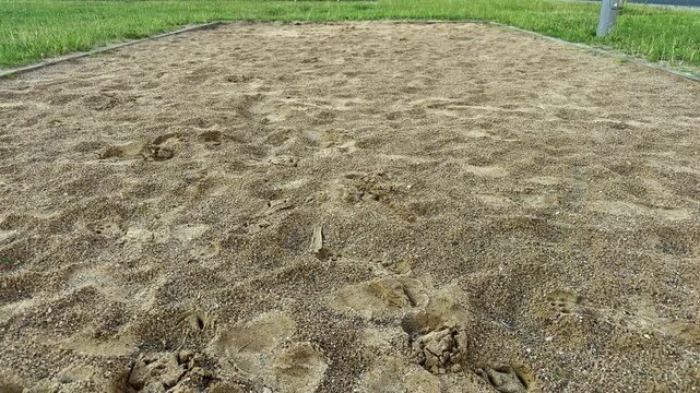 Sandy area with wooden border frame on green grass lawn, outdoor recreation space or playground pit. Sand texture, footprints, outdoor leisure, park facility