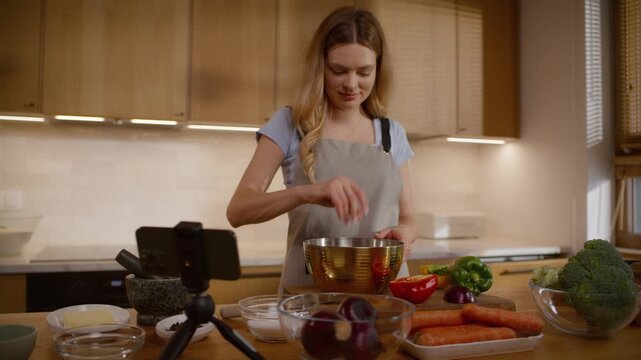 Woman learning to cook. Following the online recipe instructions displayed on her phone to make a vegan salad