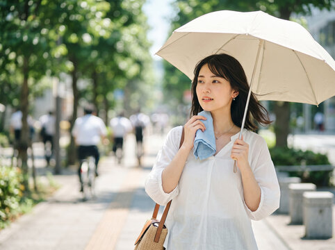 夏の街並みを日傘を差して歩きながら首元の汗をミニタオルで拭う涼しげな女性