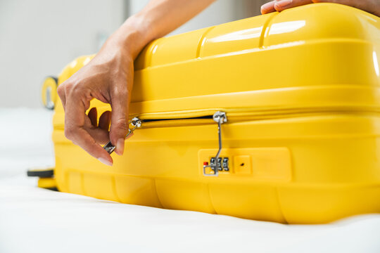 A woman's hands are zipping up a yellow wheeled suitcase after she's finished packing for her trip.
