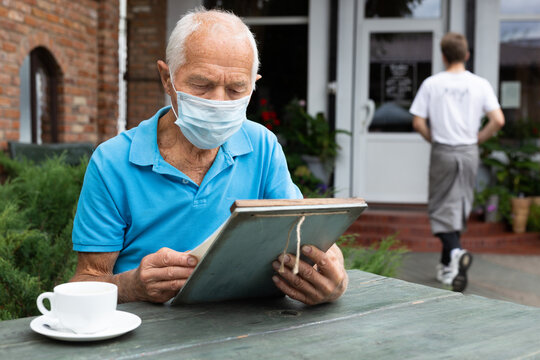 Old man in mask with menu in outdoor cafe