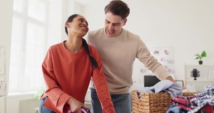 Couple ironing laundry at home with teamwork. Man and woman share chores in a bright apartment, sorting clothes and pressing shirts on a table. Clear concept of modern shared housework.