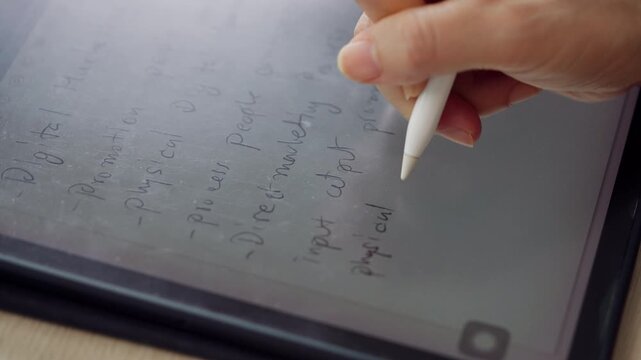 Close-up of a hand writing notes on a digital tablet using a stylus pen. Perfect for paperless workflow, digital note-taking, business planning, education, productivity, remote work, and modern techno