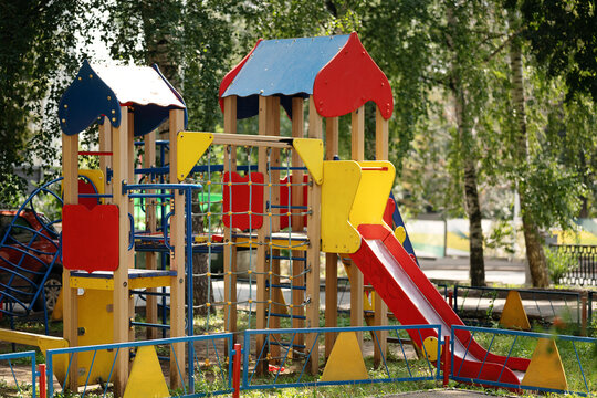 Colorful empty children playground with slides and climbing equipment in a green residential courtyard. Outdoor recreation, childhood, neighborhood amenities and family friendly urban environment.