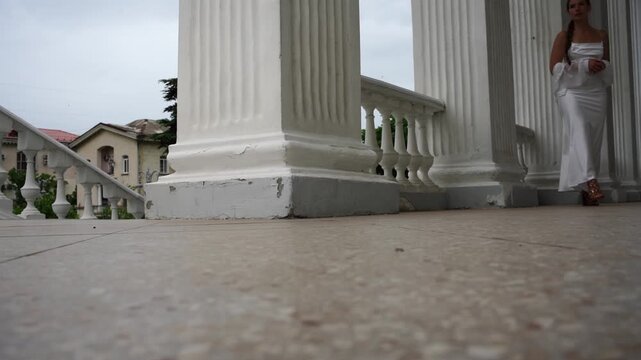 Woman white dress walking, elegant ancient colonnade terrace, classical style building facade