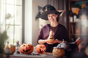 Obraz premium Smiling Woman in Witch Hat Celebrating Halloween with Pumpkins