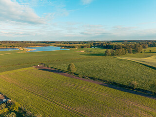 Beautiful drone capture of a rural Polish landscape in Barkoczyn, Pomerania, bathed in warm sunset light, with dramatic skies, long shadows, and endless green fields. © Lukasz