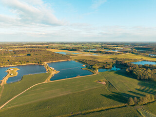 Spectacular aerial drone view of the Polish countryside in Barkoczyn, Pomerania, featuring shimmering lakes, lush green fields, winding rural roads, and a peaceful natural landscape. © Lukasz
