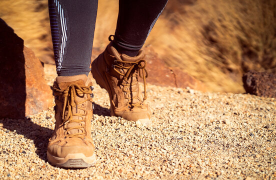 Legs in hiking boots closeup, a girl walks on a rocky desert terrain.